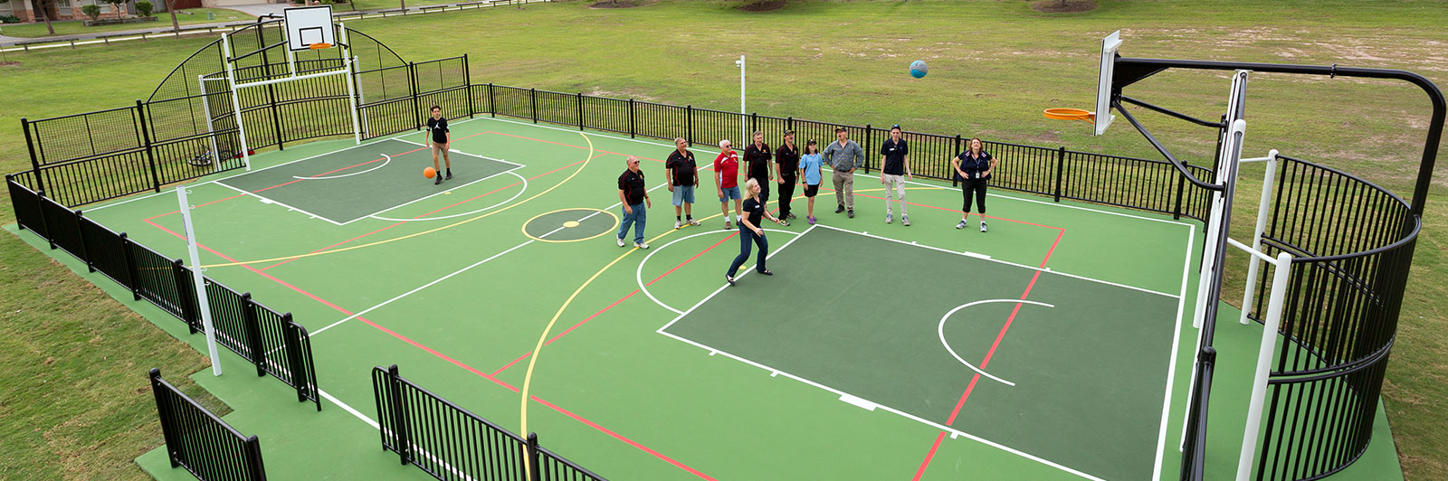 A large multi use games area, with people playing basketball inside.